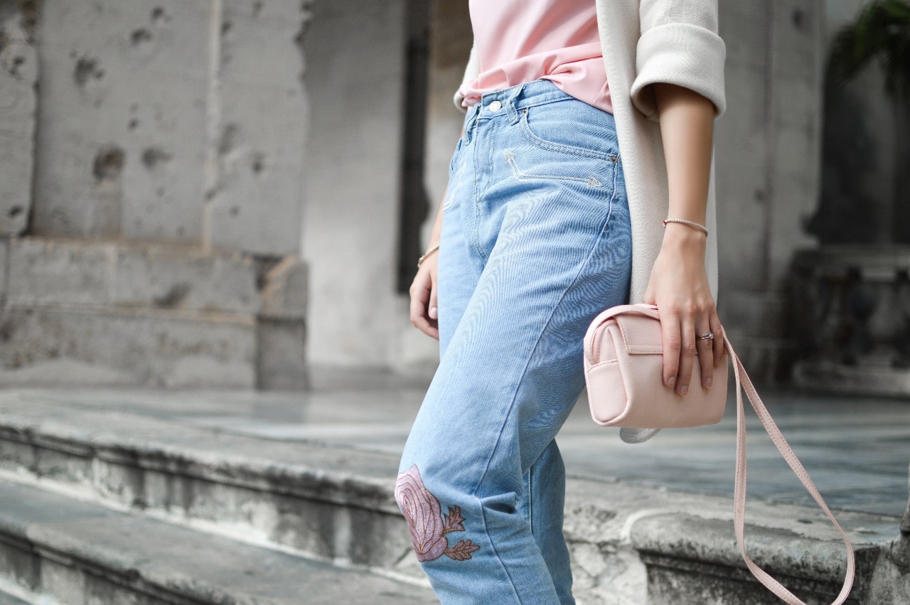 A woman clutches her pink purse while wearing white gold bangles.