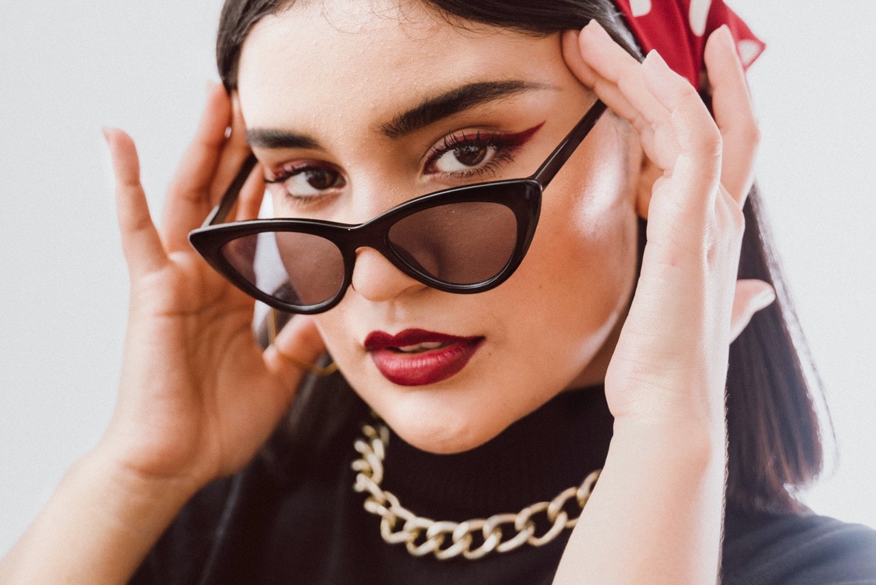 A model wearing vintage sunglasses, a black turtleneck, and a gold chain necklace.