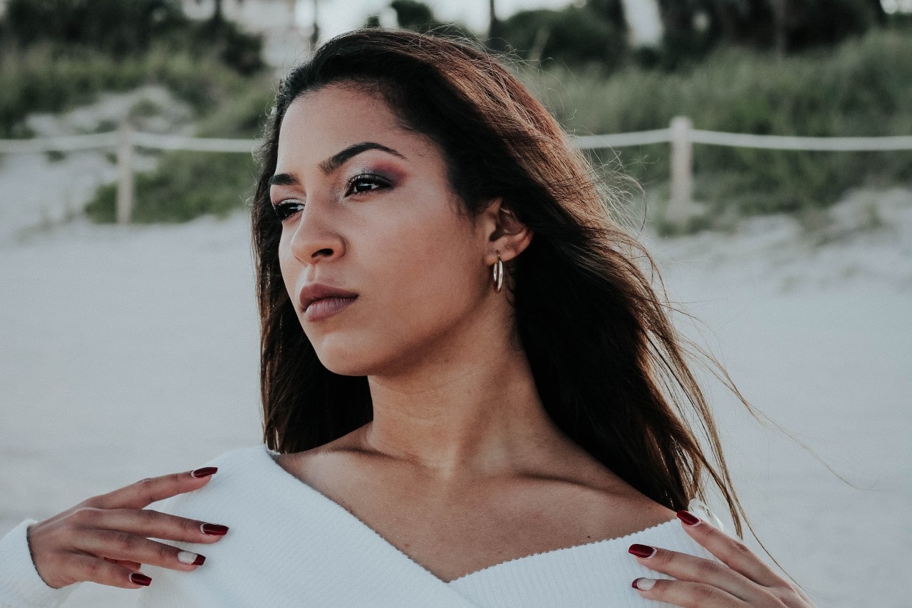 a woman on the beach looking away from the camera and wearing a pair of silver hoops