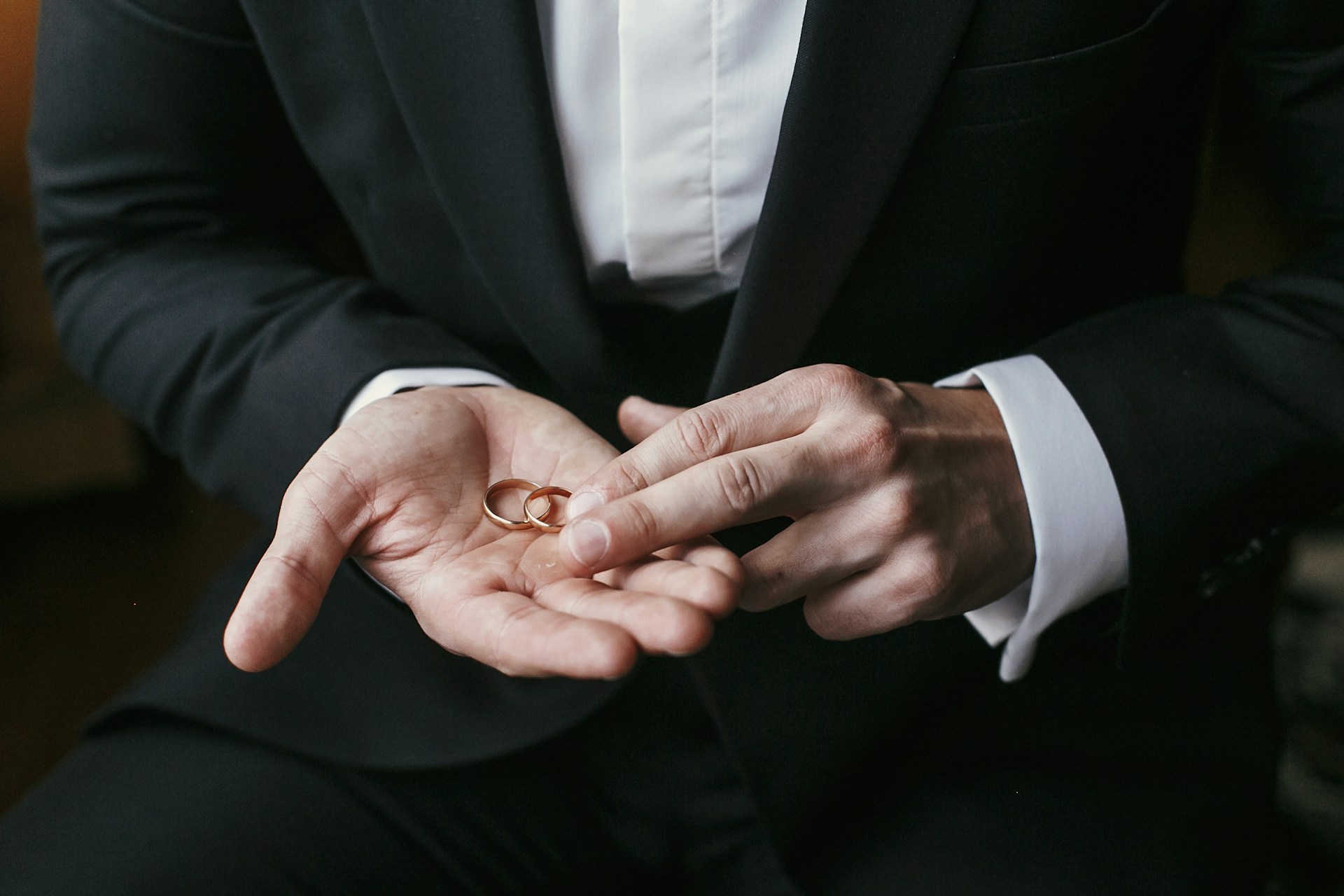 man in a suit holding two gold wedding bands in his hand