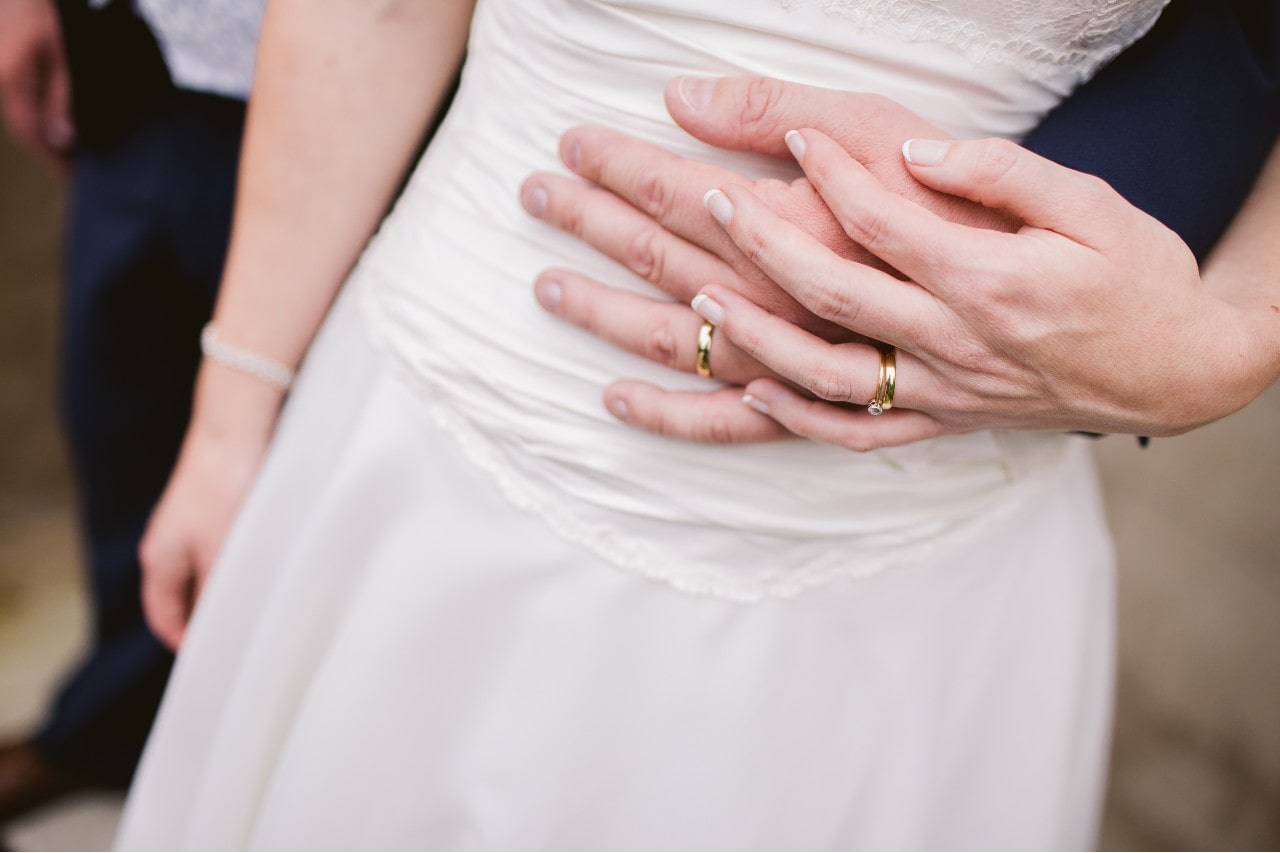 a woman and man’s hands clasping and wearing gold wedding bands