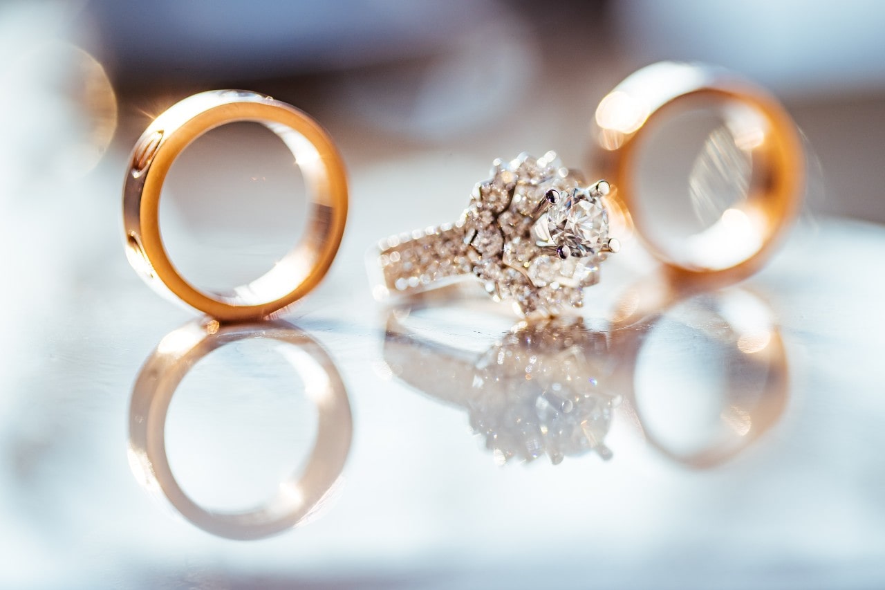 An opulent white gold engagement ring displayed between two yellow gold wedding bands.