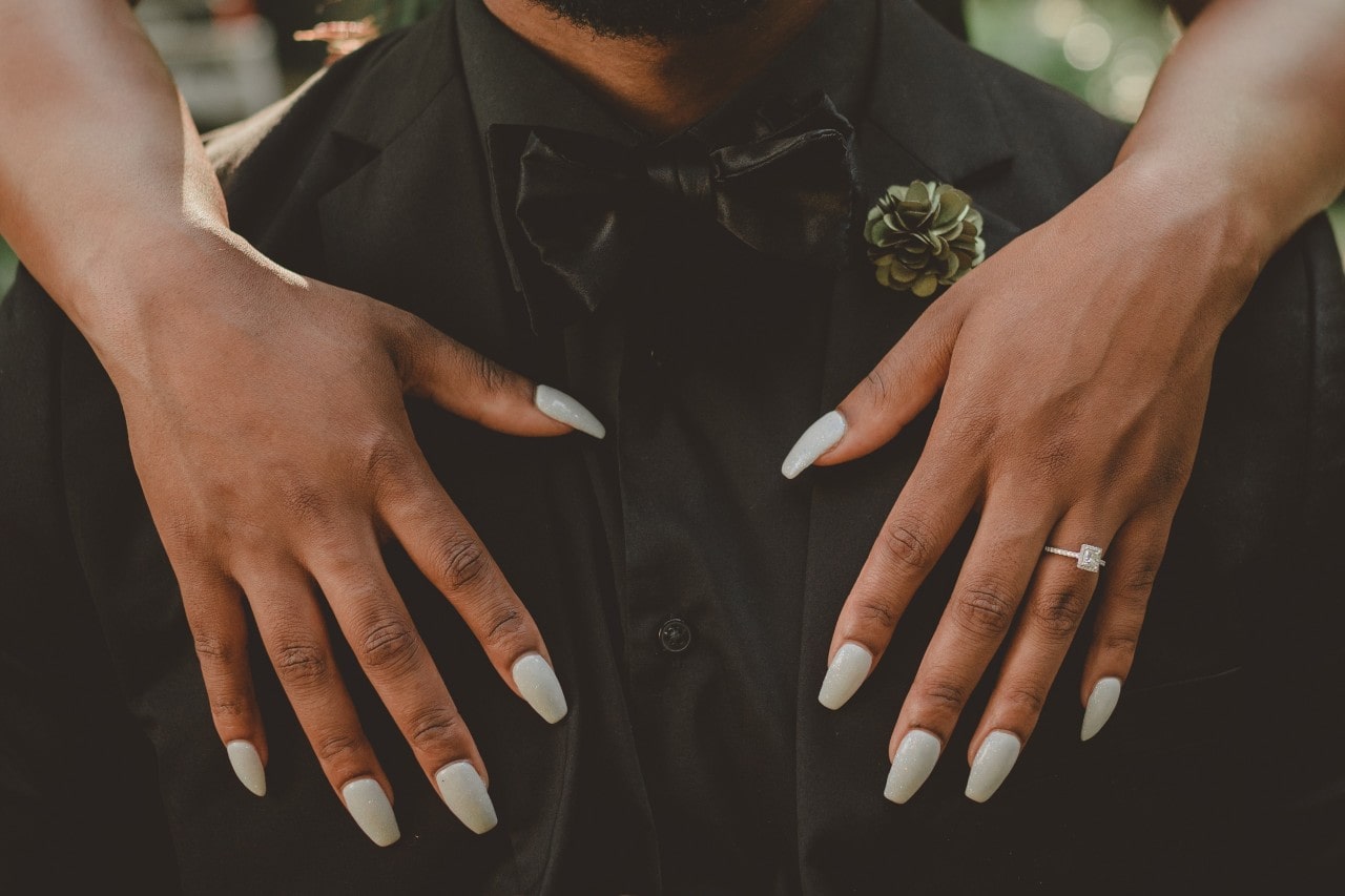 A close-up of a bride-to-be resting her hands, adorned with an elegant white gold engagement ring, on her groom’s chest.